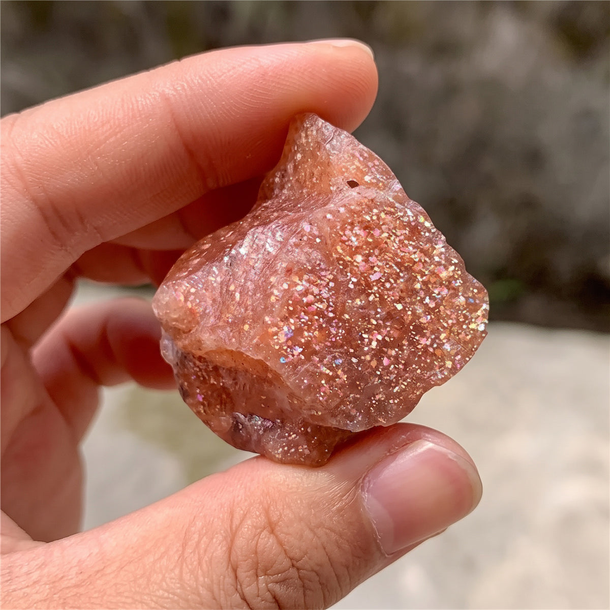 Sunstone held between fingers, sparkling in the sun